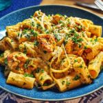 A close-up of Cowboy Butter Chicken Pasta, featuring rigatoni pasta in a creamy orange sauce with chicken pieces and parsley.