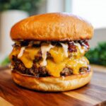 A double patty Crack Burger with melted cheddar cheese, bacon, and sauce on a brioche bun, served on a wooden board.