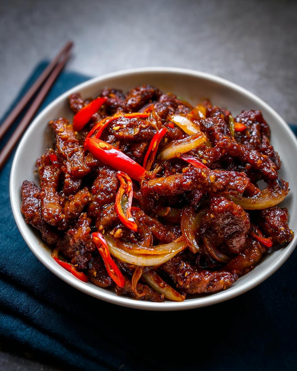 Close-up of a bowl of Crispy Chilli Beef Rice with sliced red chilies and onions.