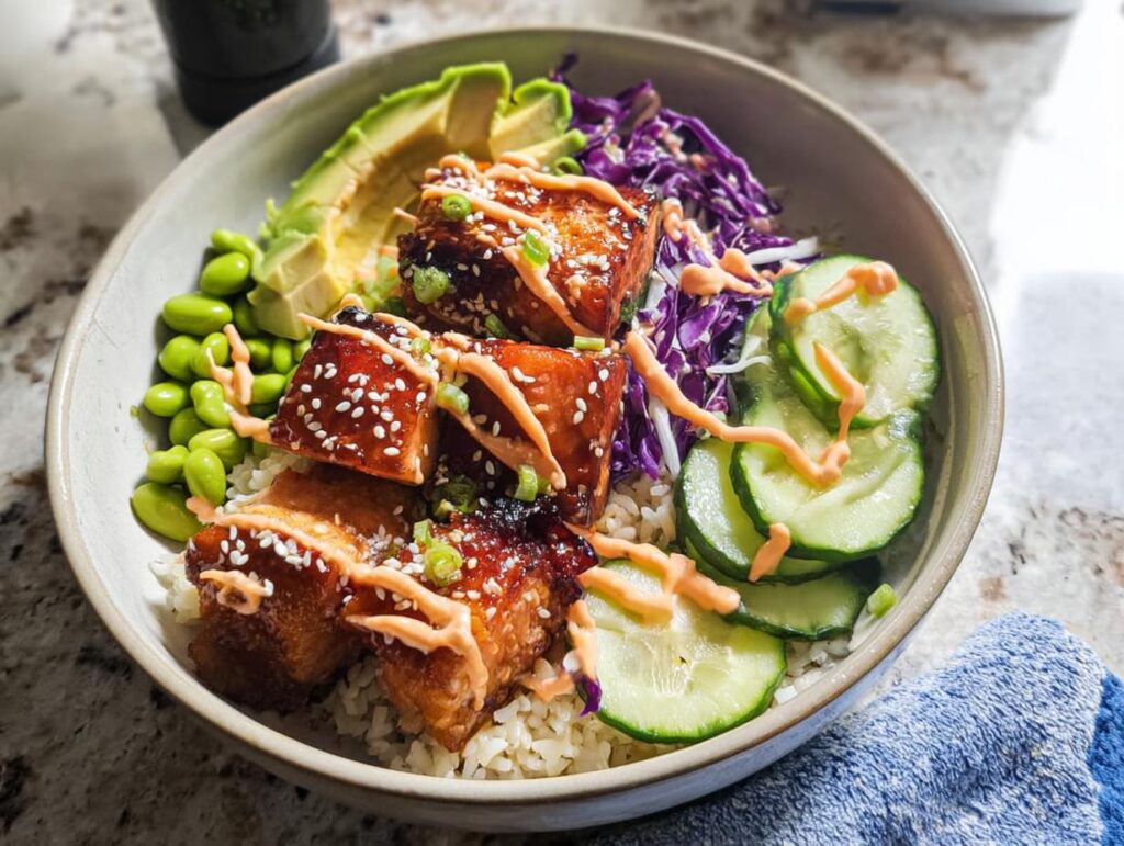 A vibrant Crispy Salmon and Rice Bowl featuring glazed salmon, edamame, avocado, cucumber, and red cabbage.
