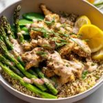 A healthy lemon garlic chicken meal prep bowl with quinoa, asparagus, and a creamy sauce.