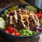 A delicious bowl filled with seasoned ground beef, lettuce, tomatoes, pickles, and cheese, drizzled with sauce. High-Protein Cheeseburger Bowls Recipe.