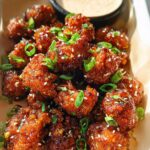 Close-up of Irresistible Sticky Honey Garlic Cauliflower bites, coated in a glossy sauce and sprinkled with sesame seeds and green onions.