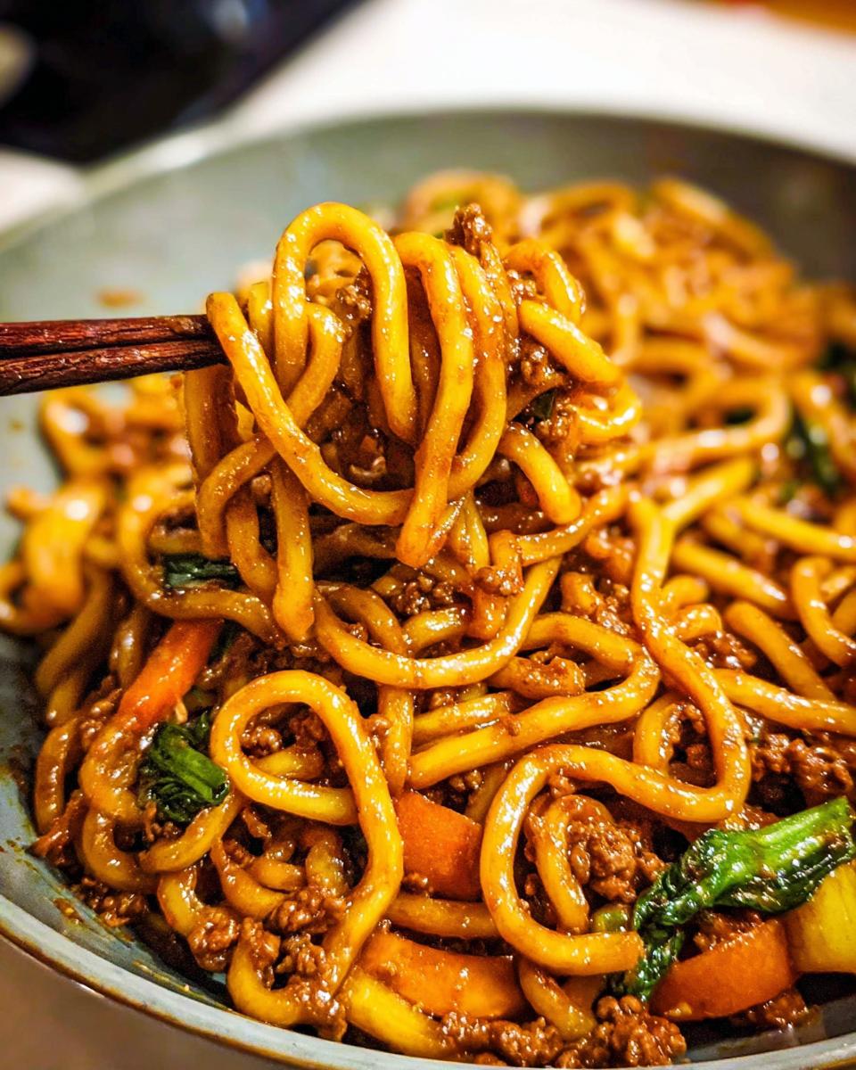 Close-up of a bowl filled with Irresistible Yaki Udon Noodles, featuring thick udon noodles coated in a savory sauce with ground meat and vegetables.