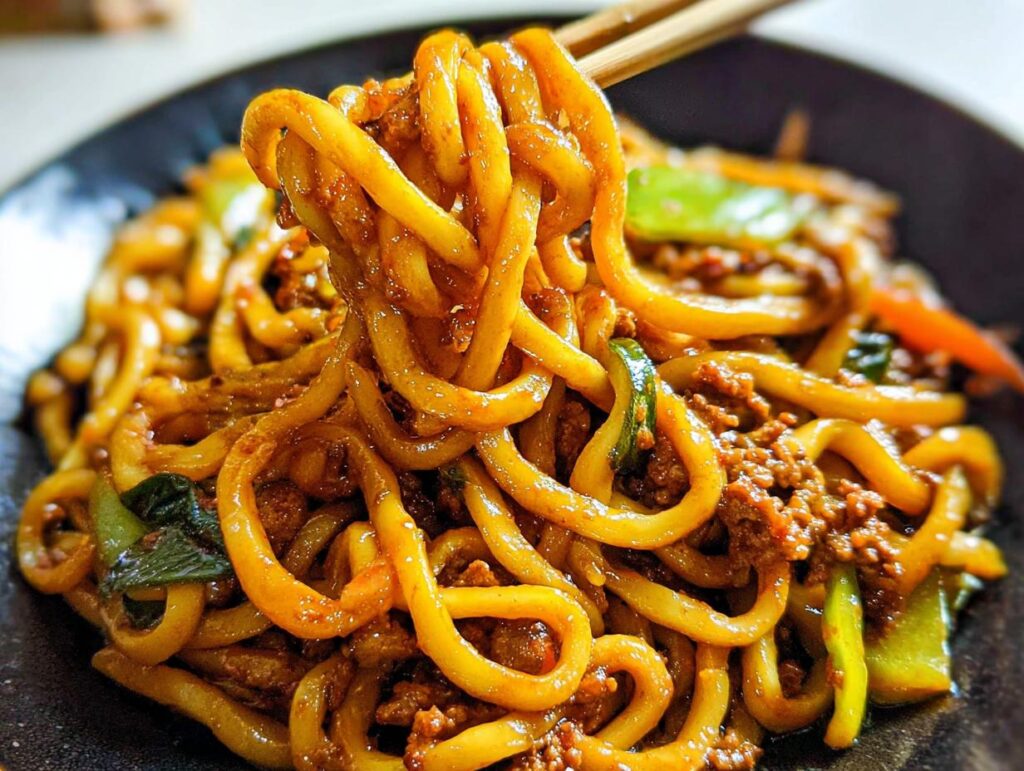 Close-up of thick, chewy udon noodles coated in a savory sauce with ground meat and vegetables in an Irresistible Yaki Udon Noodle Recipe.