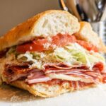 A delicious Italian Grinder Salad Sandwich overflowing with layers of salami, ham, cheese, lettuce, tomato, and dressing.