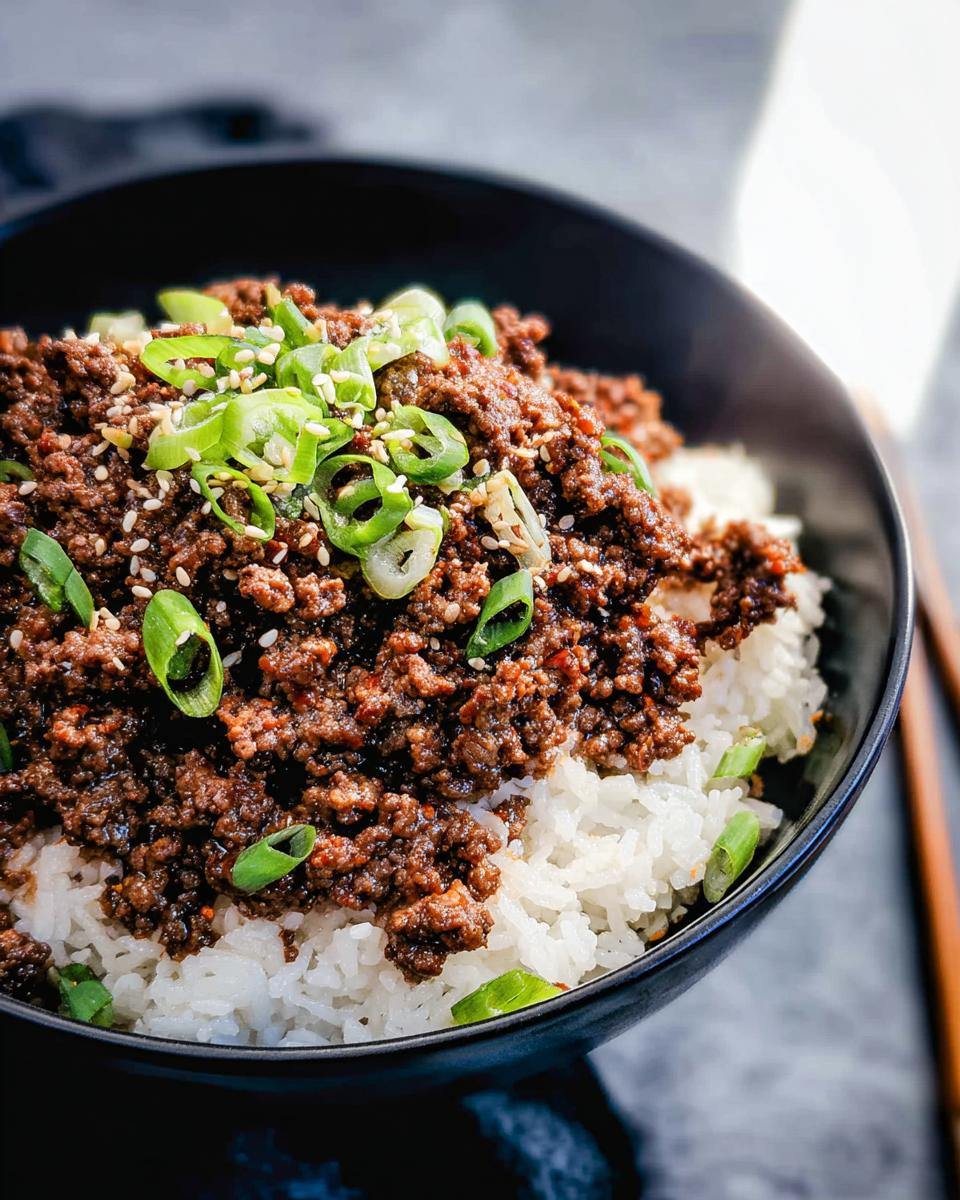 A close-up of a Korean Ground Beef Bowl, featuring seasoned ground beef over fluffy white rice, garnished with green onions and sesame seeds.