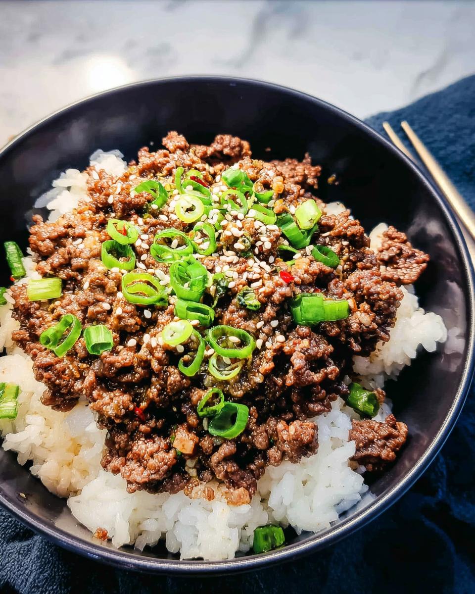 A close-up of a Korean Ground Beef Bowl, featuring seasoned ground beef over white rice, garnished with green onions and sesame seeds.