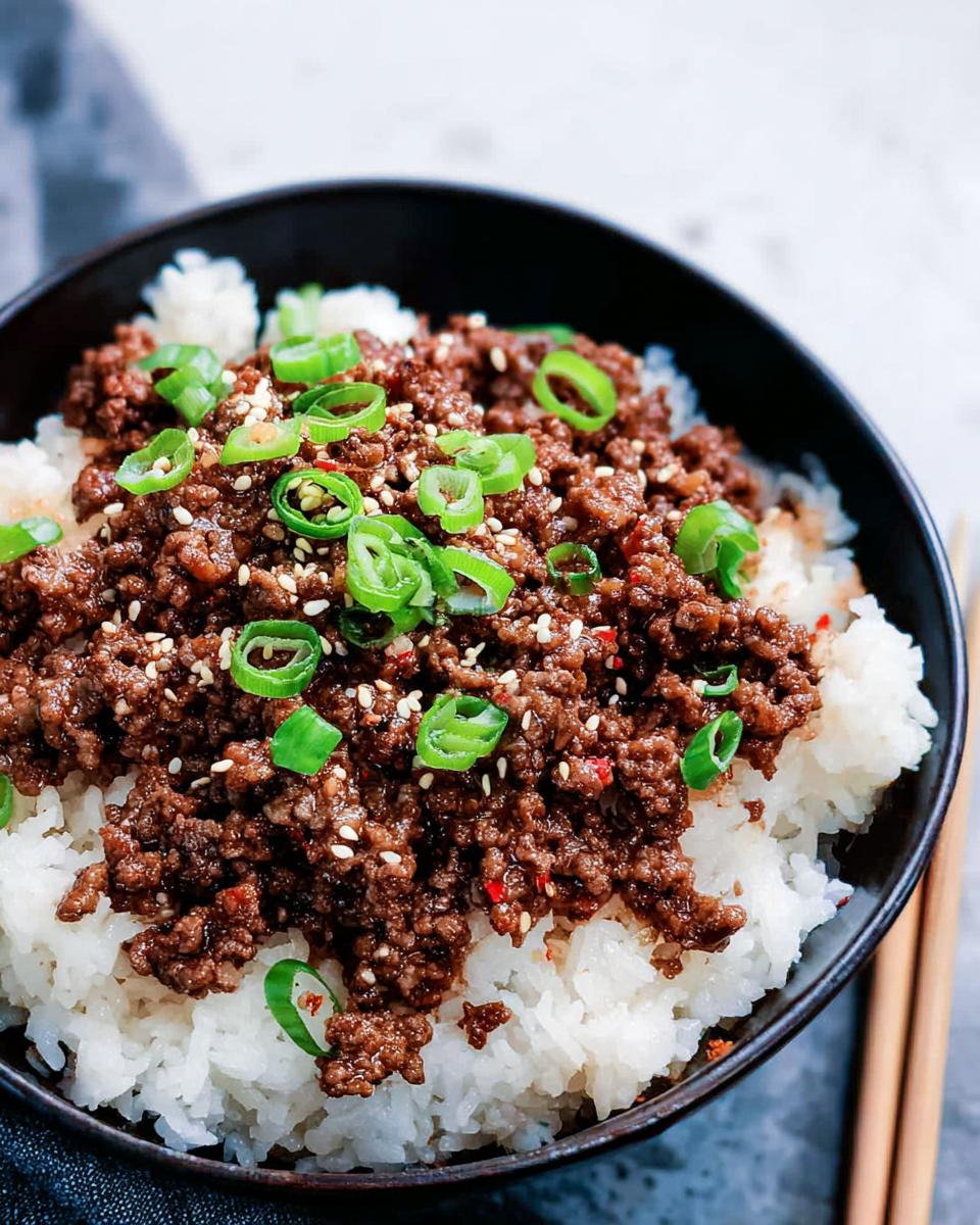 A close-up of a Korean Ground Beef Bowl, featuring seasoned ground beef over fluffy white rice, garnished with green onions and sesame seeds.