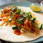 A close-up of a Sweet Chili Chicken Wrap filled with shredded chicken, cucumber, carrots, and cilantro, drizzled with sauce.