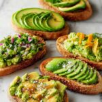 A variety of delicious avocado toast toppings on toasted bread, including sliced avocado, mashed avocado with herbs, and avocado with citrus zest.