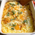 A close-up view of baked feta eggs in a white casserole dish, topped with fresh basil and cracked black pepper.