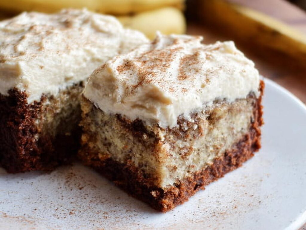 Close-up of two slices of Banana Bread Brownies Made Easy, topped with creamy frosting and a sprinkle of cinnamon.
