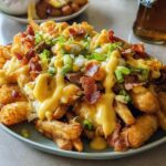 A plate of Breakfast Poutine with Hollandaise Sauce, featuring crispy fries, tater tots, bacon, and green onions.