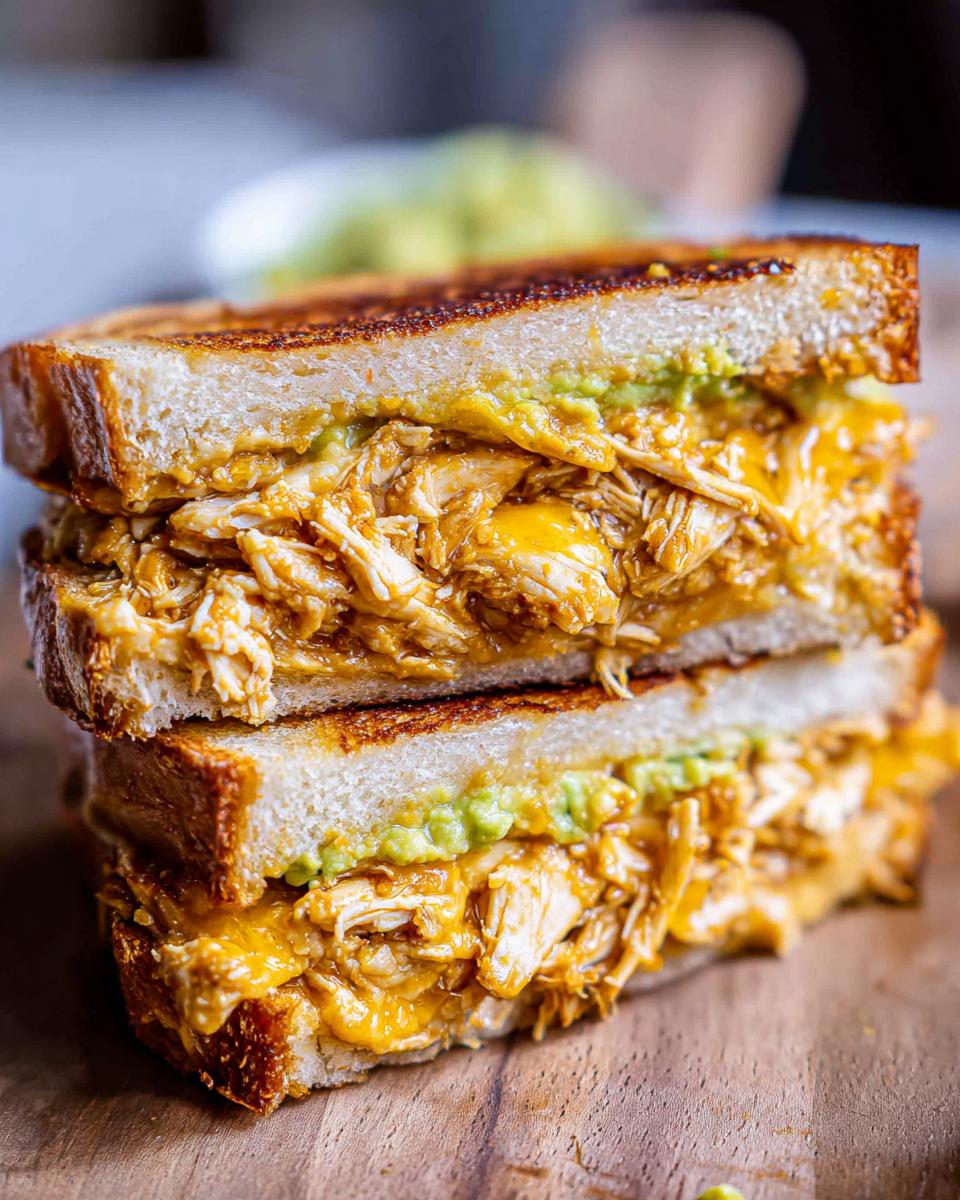 A close-up of a stacked Chicken Avocado Melt Sandwich, showing shredded chicken, melted cheese, and avocado on toasted bread.