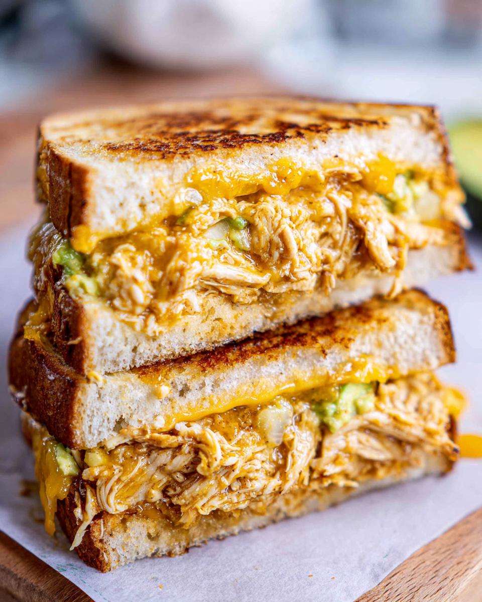 A close-up of a stacked Chicken Avocado Melt Sandwich with melted cheese and shredded chicken.
