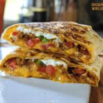 A cross-section of a delicious Chicken Crunch Wrap, showing shredded chicken, melted cheese, tomatoes, and sour cream.