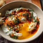 A bowl of Çılbır, Turkish eggs with creamy yogurt, drizzled with chili butter sauce and fresh dill, served with crusty bread.