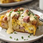 A delicious slice of Easy Eggs Benedict Casserole topped with creamy hollandaise sauce, diced ham, and chives.