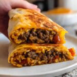 A close-up of an Easy Grilled Cheese Burrito Copycat Recipe, cut in half to show the seasoned ground beef and rice filling.