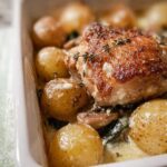 Close-up of golden brown Garlic Parmesan Chicken Thighs and Potatoes in a creamy sauce, garnished with thyme.
