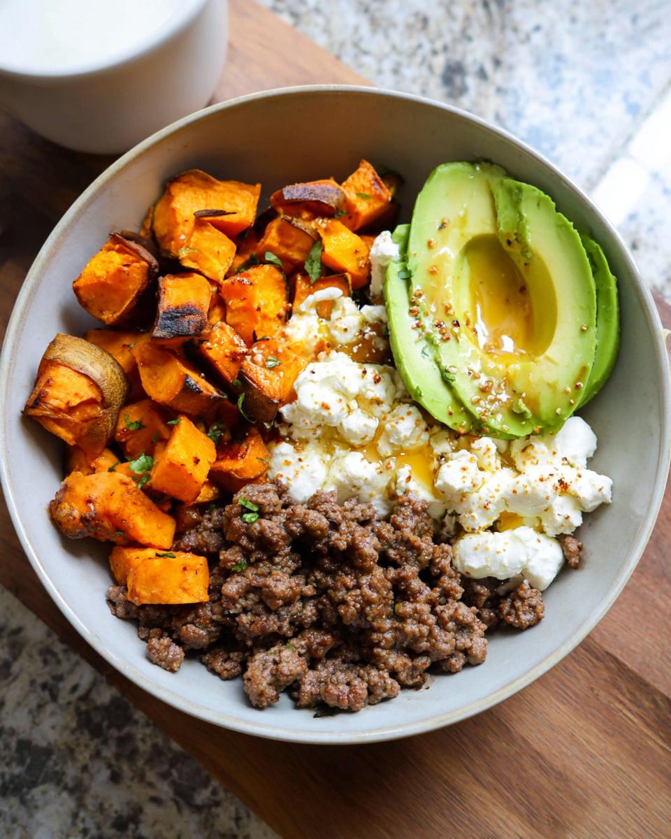 A delicious Ground Beef Hot Honey Bowl featuring seasoned ground beef, roasted sweet potatoes, creamy cottage cheese, and sliced avocado drizzled with honey.