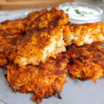 A plate of golden-brown, crispy Healthy Sweet Potato Hash Browns served with a side of dipping sauce.