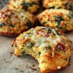 Close-up of a High Protein Breakfast Biscuit with melted cheese, spinach, and red bits, one biscuit has a bite taken out.