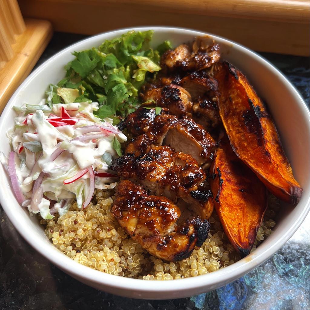 A delicious Hot Honey Chicken Bowl featuring glazed chicken, roasted sweet potato wedges, quinoa, and a fresh slaw.
