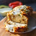 A slice of juicy garlic parmesan chicken meatloaf topped with melted cheese, served on a plate.