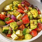 A bowl of Simple & Zesty Mediterranean Avocado Egg Salad with diced avocado, tomatoes, cucumber, red onion, olives, and feta cheese.