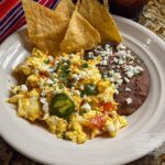 Scrambled Mexican Eggs with diced tomatoes, jalapeños, crumbled cheese, refried beans, and tortilla chips.