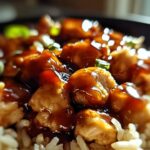 Close-up of tender chicken pieces coated in glossy honey BBQ sauce served over fluffy rice, garnished with green onions.
