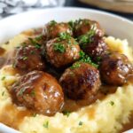 A bowl of Salisbury steak meatballs served over creamy garlic herb mashed potatoes, garnished with parsley.