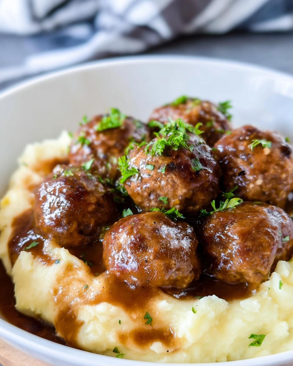 A bowl of Salisbury Steak Meatballs with Garlic Herb Mashed Potatoes, garnished with fresh parsley.