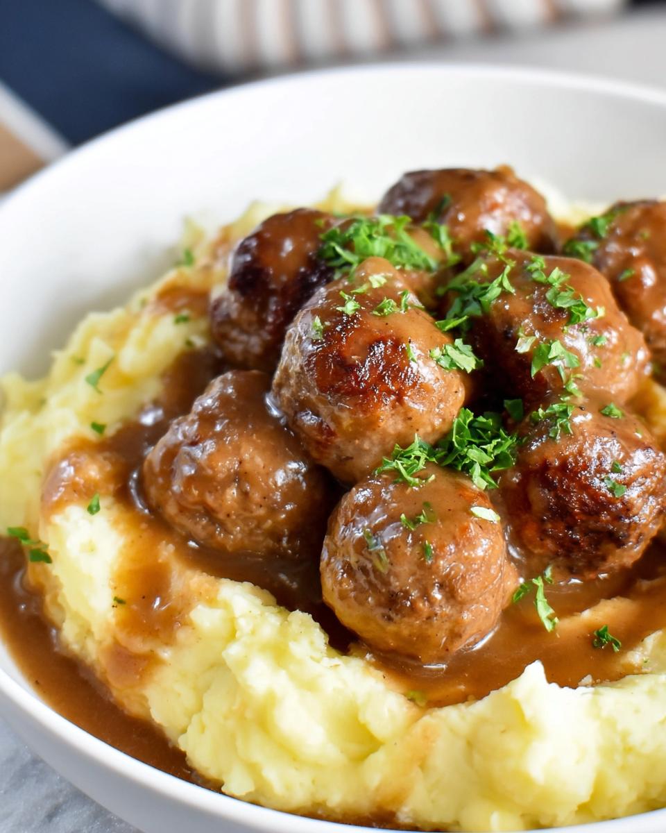 Close-up of Salisbury Steak Meatballs nestled in creamy garlic herb mashed potatoes, garnished with parsley.