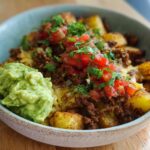 A close-up of a Schnelle Kartoffel Taco Bowl Meal Prep, featuring seasoned potatoes, ground meat, melted cheese, pico de gallo, and guacamole.