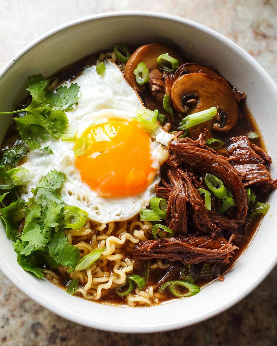 A close-up of a bowl of Slow Cooker Beef Ramen Noodles topped with a fried egg, mushrooms, cilantro, and green onions.