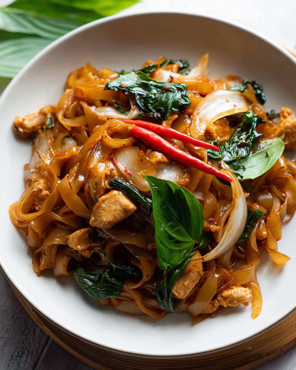Close-up of Street Style Thai Drunken Noodles with chicken, basil, onions, and red chilies.