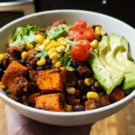 A vibrant Sweet Potato Taco Bowl filled with roasted sweet potatoes, black beans, corn, cherry tomatoes, avocado slices, and shredded lettuce.