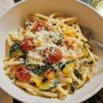 A bowl of delicious Tomato Zucchini Pasta, topped with grated cheese and fresh herbs.