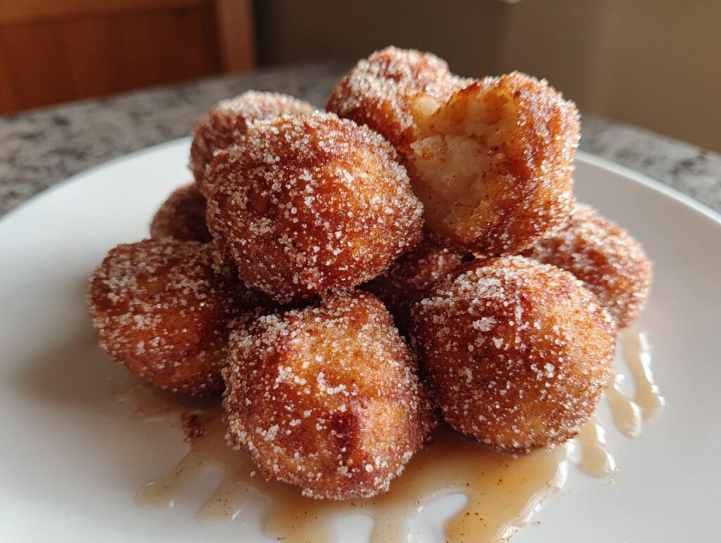 A pile of golden brown air fryer donut holes coated in cinnamon sugar, with one hole broken open.