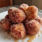 A pile of golden brown air fryer donut holes coated in cinnamon sugar, with one hole broken open.
