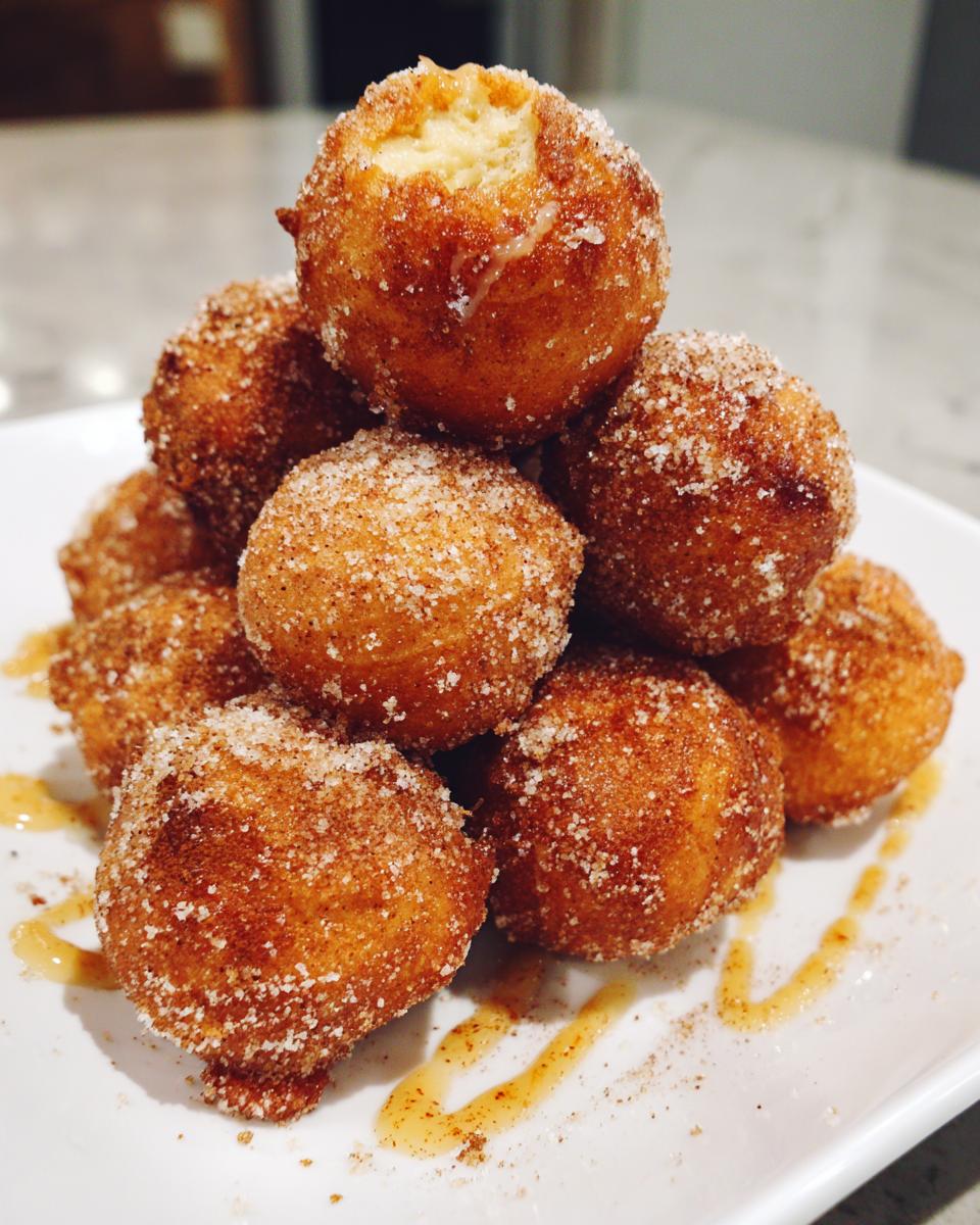 A stack of golden brown air fryer cinnamon sugar donut holes drizzled with honey on a white plate.