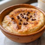 A close-up of a baked protein pancake bowl topped with chocolate chips and a drizzle of syrup.