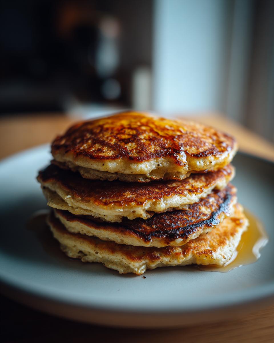 A stack of fluffy banana oat pancakes drizzled with syrup on a light grey plate.