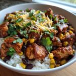 A close-up of a delicious BBQ chicken bowl with rice, black beans, corn, shredded cheese, and cilantro.