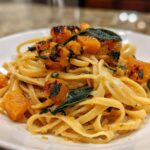 Close-up of fettuccine pasta tossed with creamy sauce, topped with roasted butternut squash cubes and crispy sage leaves.