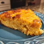 A slice of cheesy hash brown casserole on a blue plate, perfect for breakfast.