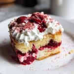 A slice of Cherry Amaretto Tiramisu on a white plate, featuring layers of cake, cream, and cherries, topped with whipped cream and cherries.